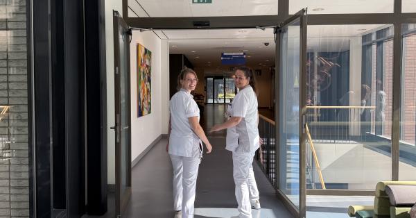 Twee verpleegkundigen lopen door de gang en kijken om